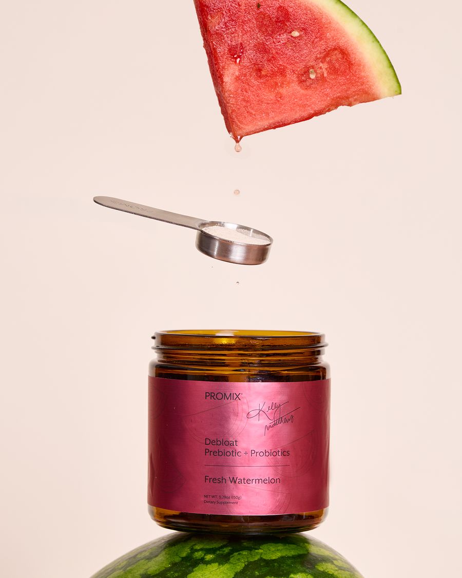 A jar of Promix Debloat Prebiotic + Probiotics in Fresh Watermelon with a measuring scoop and a watermelon wedge suspended above it