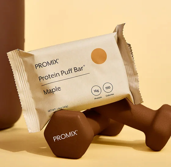 Promix Maple Protein Puff Bar leaning against dumbbells beside a water bottle