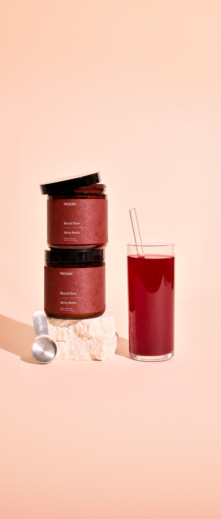 Two jars of Blood Flow Berry Beets on a stone, a scoop and a glass of the drink